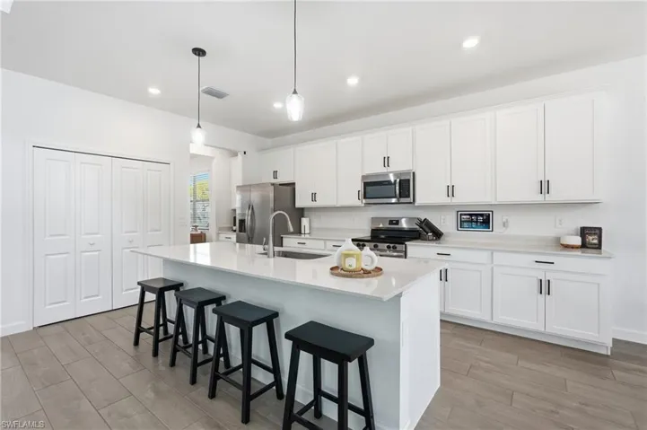 Bright kitchen featuring a substantial island with countertop seating, white shaker cabinetry with black hardware, stainless steel appliances, pendant lighting, and wood-finish flooring