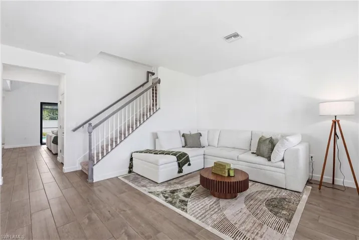Spacious living area featuring wood-finish flooring, a white staircase with grey handrails, and crisp white walls