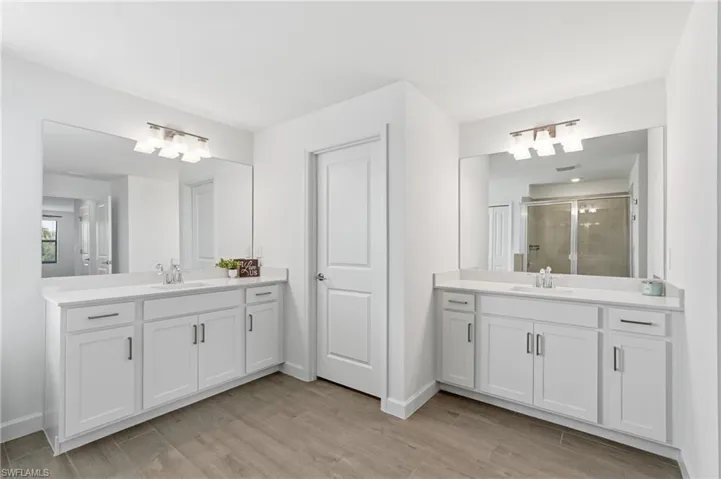 Dual white vanities with integrated sinks, quartz-finish countertops, wood-finish flooring, and large wall-mounted mirrors