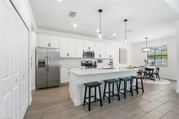 Modern kitchen featuring white cabinetry with black hardware, stainless steel appliances, a center island with countertop seating, and wood-finish flooring