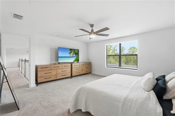 Spacious room featuring neutral carpeting, a ceiling fan with integrated lighting, a large window with horizontal blinds, and a hallway entry with railing