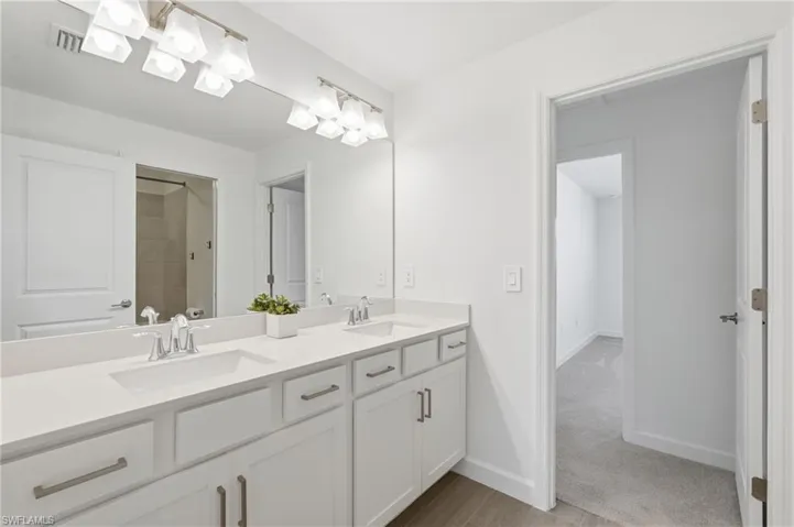 Second Floor- Double vanity with integrated sinks, white cabinetry, chrome fixtures, and a full-width mirror with dual sconce lighting