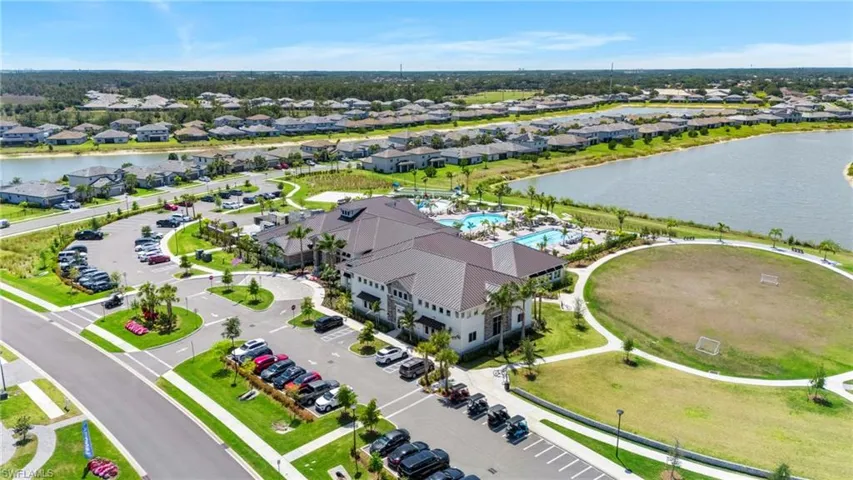 Community clubhouse with a large swimming pool, expansive green spaces, paved walking paths, and multiple parking areas