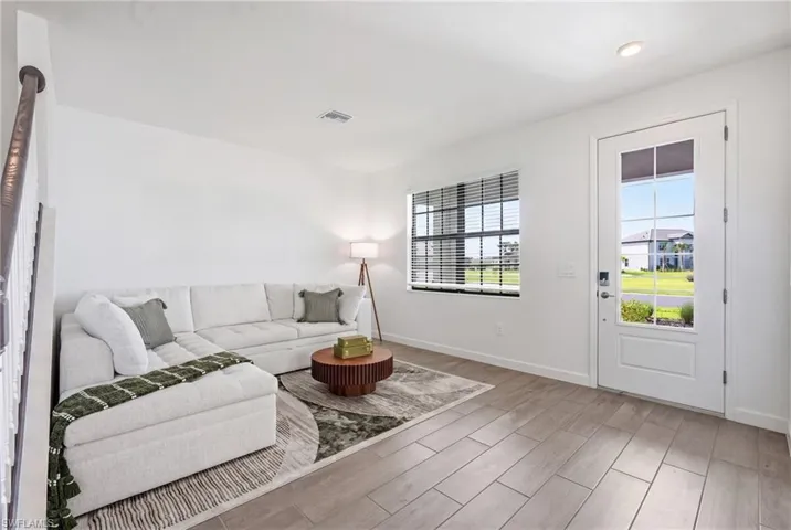Bright living space featuring wood-finish flooring, a contemporary entrance door with glass panels, and a large window with horizontal blinds