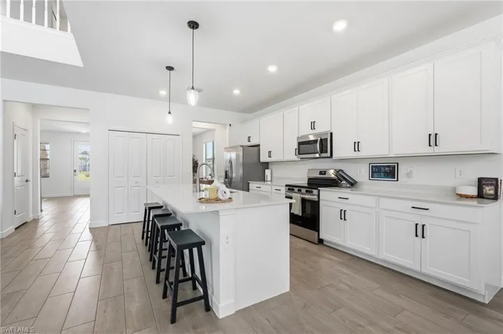 Spacious kitchen featuring an expansive island with pendant lighting, white shaker-style cabinetry, stainless steel appliances, and light-toned countertops