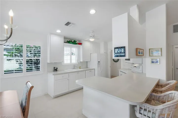 Kitchen featuring Plantation Shutters, a breakfast bar area, a peninsula, white appliances, and white cabinetry