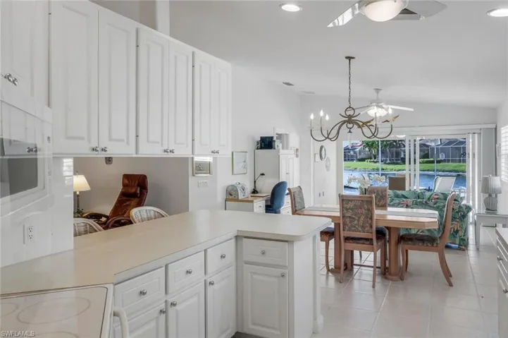 Kitchen with white electric range, light countertops, white cabinets, decorative light fixtures, and a peninsula