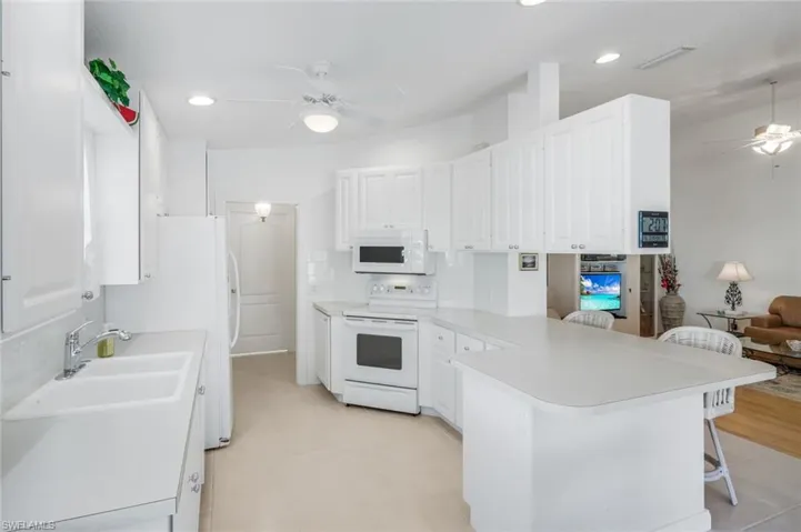 Kitchen with ceiling fan, white appliances, a breakfast bar, white cabinets, and light countertops