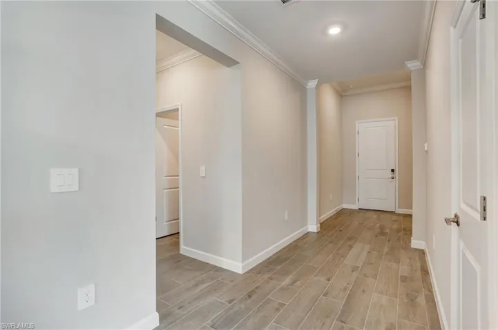 Hall with crown molding, baseboards, and light wood-style floors