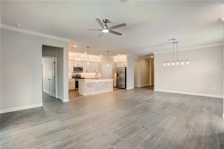 Unfurnished living room with a sink, ceiling fan, baseboards, ornamental molding, and light wood-type flooring