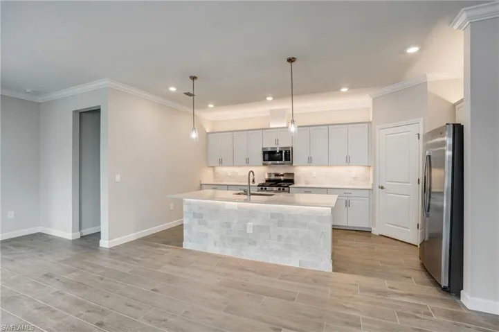 Kitchen with stainless steel appliances, baseboards, light countertops, light wood-style flooring, and crown molding