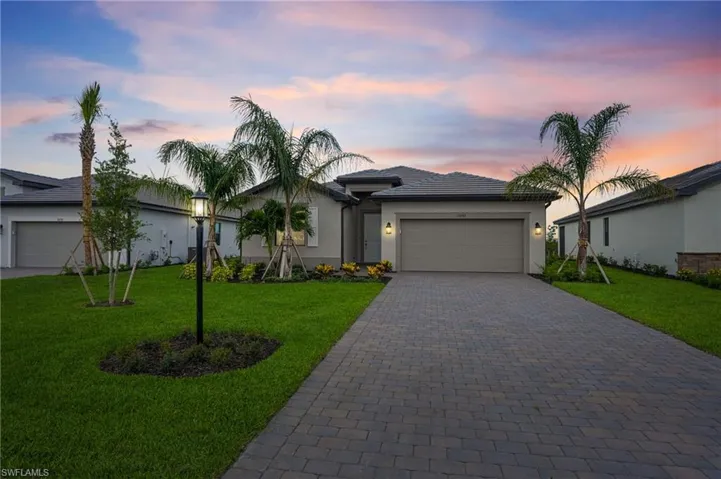 Single story home with decorative driveway, an attached garage, stucco siding, a front lawn, and a tiled roof
