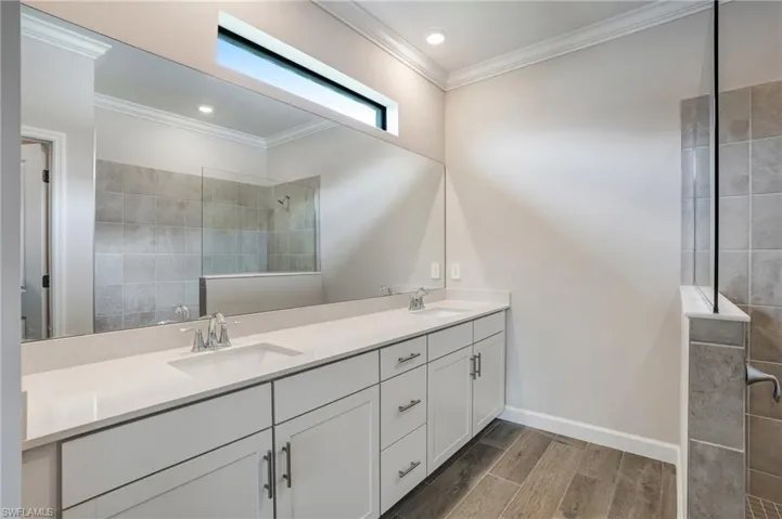 Bathroom featuring double vanity, wood finish floors, crown molding, walk in shower, and baseboards