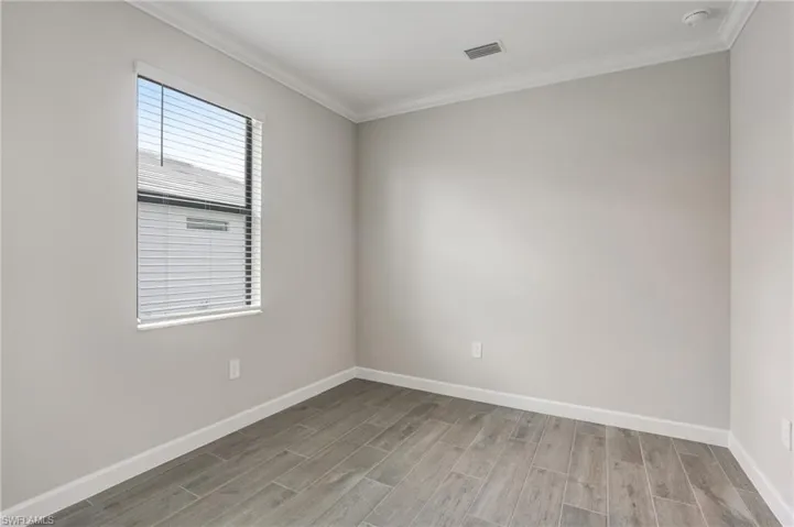 Unfurnished room with wood finished floors, baseboards, crown molding, and a smoke detector