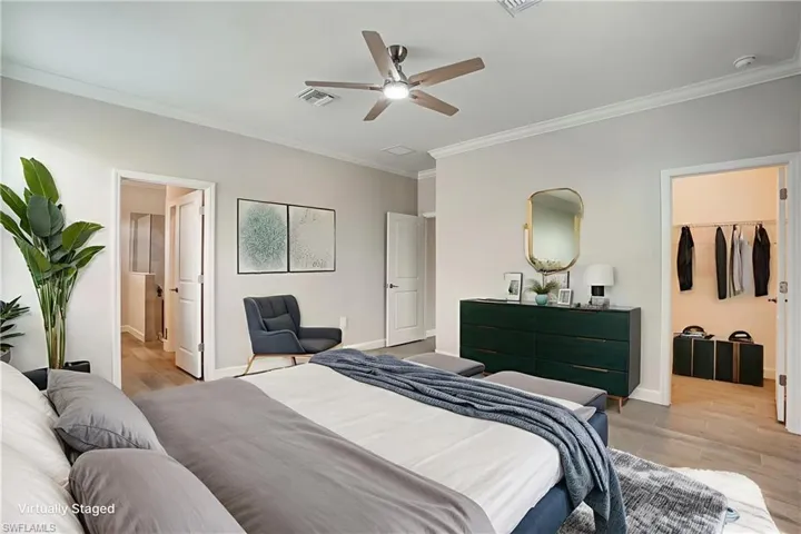 Bedroom with ornamental molding, light wood-type flooring, baseboards, a spacious closet, and ensuite bathroom