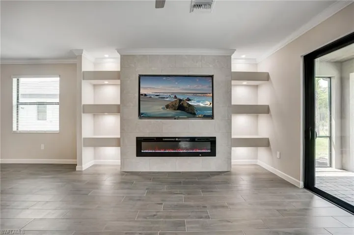 Unfurnished living room with ornamental molding, baseboards, wood finish floors, built in features, and a tiled fireplace