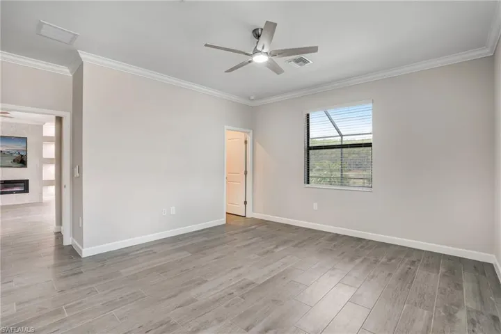 Empty room featuring a ceiling fan, wood finished floors, crown molding, and baseboards