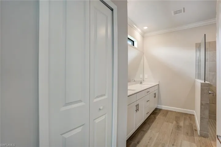 Bathroom featuring double vanity, ornamental molding, wood finished floors, walk in shower, and baseboards