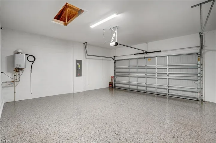 Garage featuring electric panel, a garage door opener, and tankless water heater