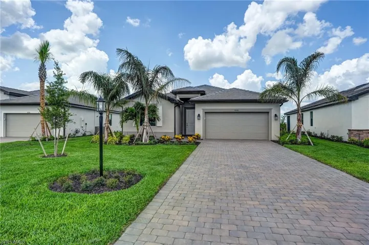 Ranch-style home with a garage, stucco siding, decorative driveway, and a front yard