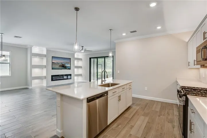 Kitchen with stainless steel appliances, a sink, open floor plan, light wood-style flooring, and crown molding