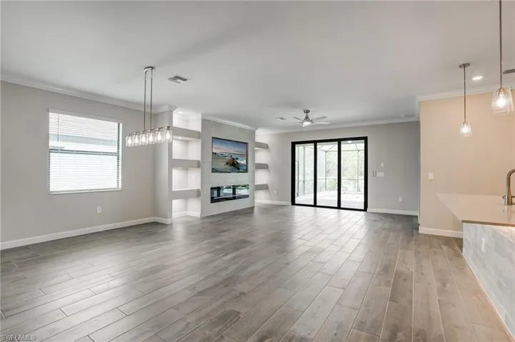 Unfurnished living room with wood finished floors, crown molding, a tiled fireplace, ceiling fan, and baseboards