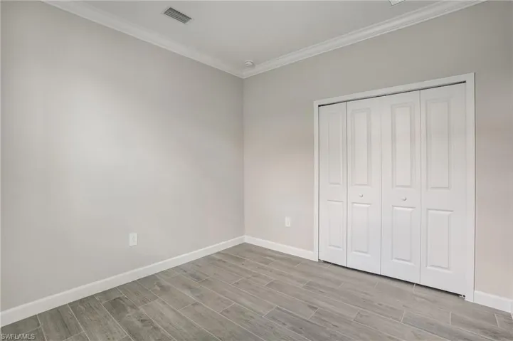 Unfurnished bedroom featuring light wood-type flooring, baseboards, crown molding, and a closet