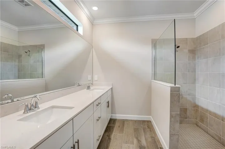 Full bath with double vanity, a walk in shower, crown molding, wood finished floors, and baseboards