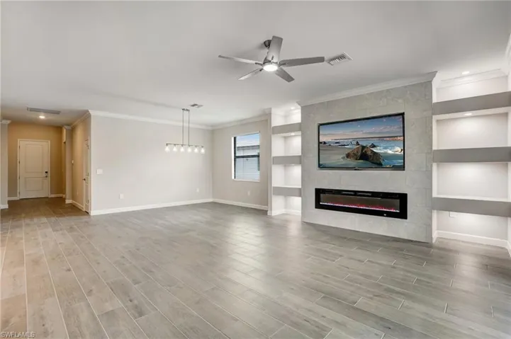 Unfurnished living room featuring baseboards, crown molding, ceiling fan, a tiled fireplace, and built in shelves