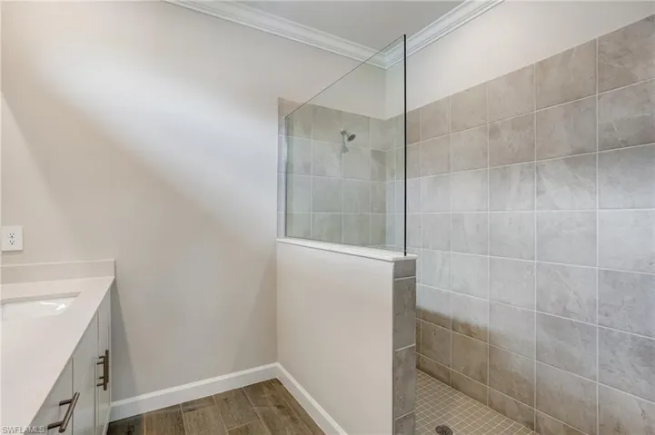 Full bath with crown molding, walk in shower, vanity, baseboards, and wood finished floors