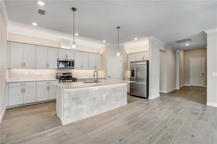 Kitchen with appliances with stainless steel finishes, a sink, backsplash, light countertops, and crown molding