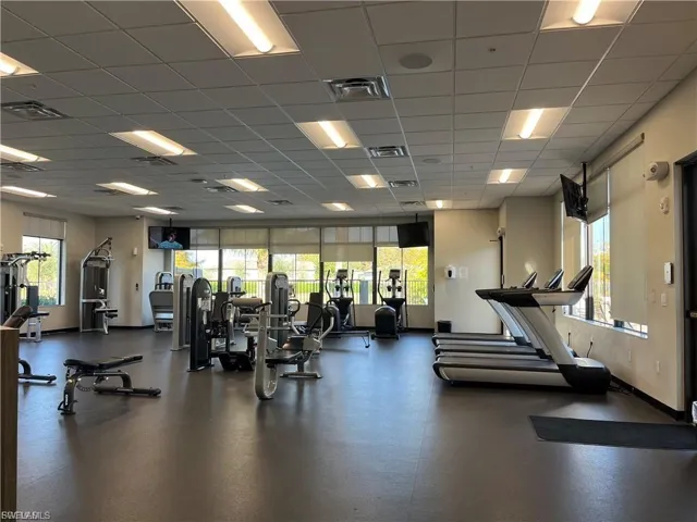 Spacious fitness center featuring a rubberized floor, multiple treadmills, strength training equipment, large windows with roller shades, and recessed lighting