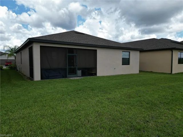 Expansive rear yard featuring a large screened-in patio, stucco exterior, dark roof shingles, and green lawn space