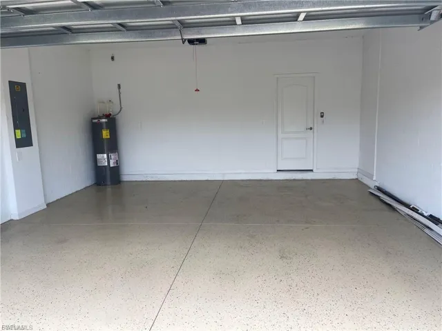 Spacious garage featuring white painted walls, a textured light-toned epoxy floor, and a white interior door with a paneled design
