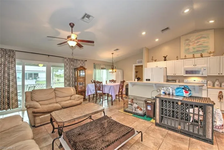Tiled living room featuring ceiling fan with notable chandelier and vaulted ceiling