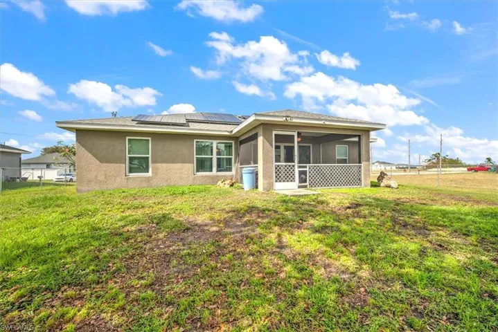Rear view of property with a sunroom, a lawn, and solar panels