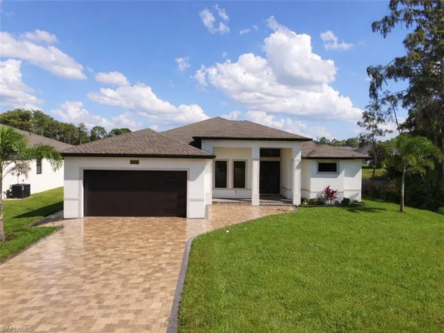 Modern stucco exterior featuring a dark brown garage door, a front entry with a dark door and sidelights, a paver driveway, and a shingle roof