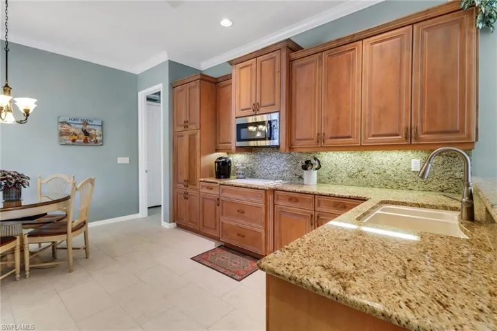 Kitchen featuring brown cabinets, hanging light fixtures, a sink, light stone countertops, and stainless steel microwave