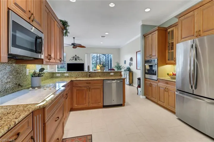 Kitchen with brown cabinets, glass insert cabinets, a sink, stainless steel appliances, and a peninsula