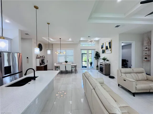 Living room featuring a raised ceiling, a ceiling fan, french doors, a chandelier, and beamed ceiling