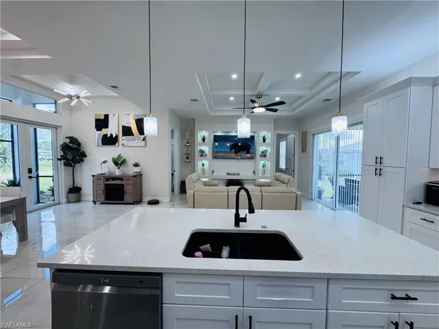 Kitchen featuring a ceiling fan, pendant lighting, open floor plan, light stone countertops, and beam ceiling