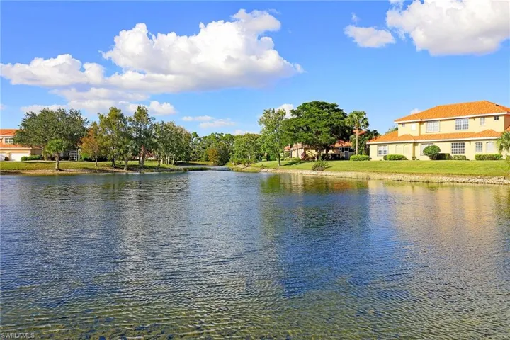 Waterfront property featuring a retention pond, manicured turf, mature trees, and a two-story residence with a tile roof