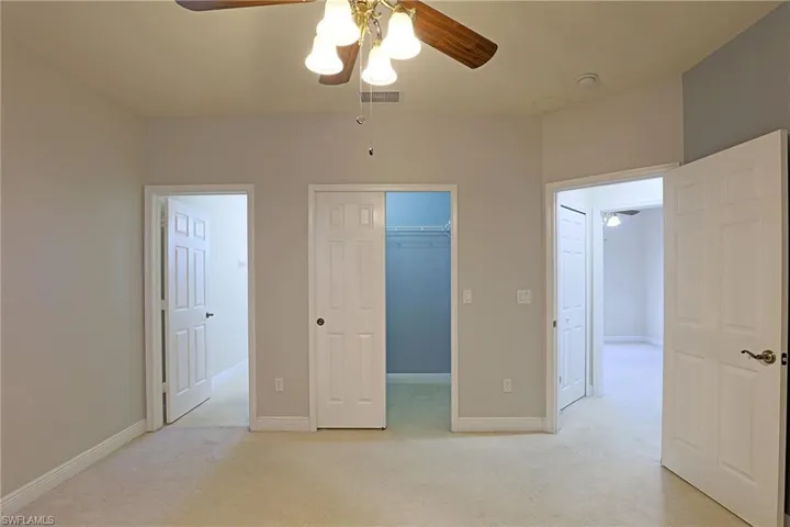 Neutral-toned room featuring carpeted flooring, a ceiling fan with multi-light fixture, and a reach-in closet with wire shelving