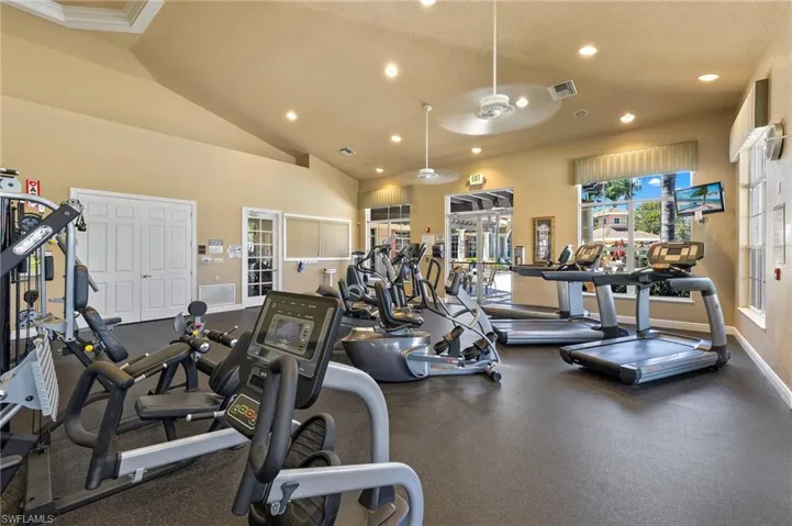 Fitness center featuring vaulted ceilings, recessed lighting, dual ceiling fans, large windows, and rubberized flooring