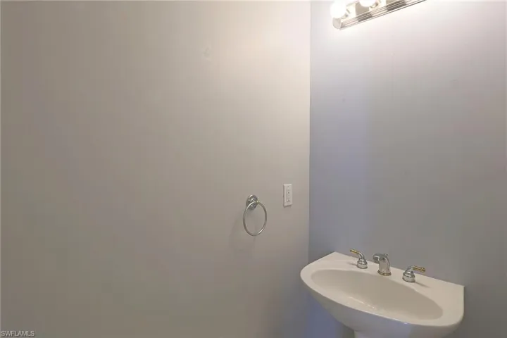Wall-mounted pedestal sink featuring a multi-handle faucet, accompanied by a circular wall-mounted towel ring and a three-bulb vanity light fixture