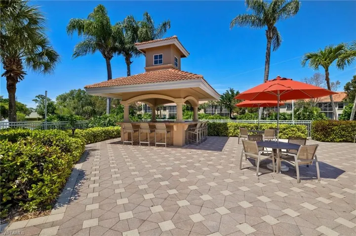 Outdoor pavilion featuring a tiled roof and built-in bar, set on a geometric paver patio surrounded by mature palms and manicured hedges