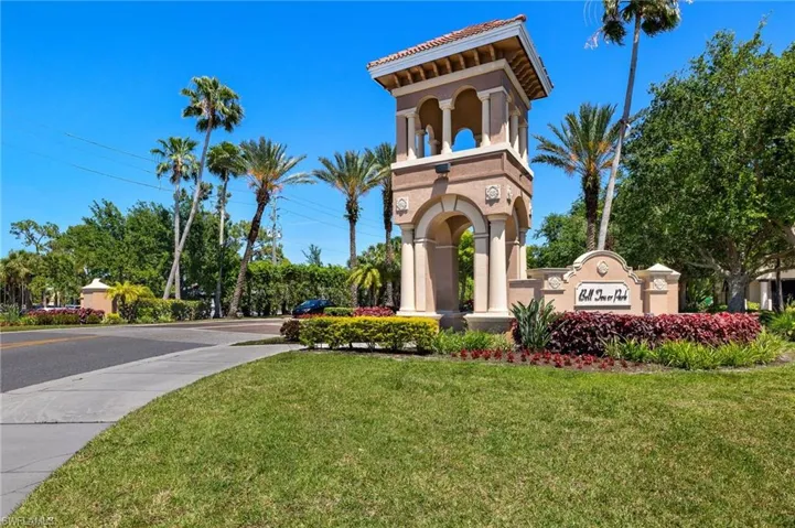 Stucco architectural tower featuring arched detailing, column accents, and a tile roof, situated amidst manicured landscaping with mature palm trees