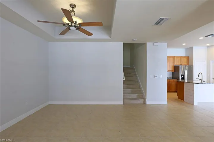 Open-concept interior featuring tile flooring, a tray ceiling with a mounted light-integrated ceiling fan, carpeted staircase, and kitchen with wood cabinetry and stone-surfaced island