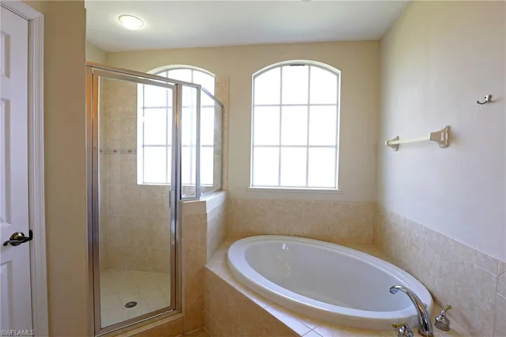 Bathroom featuring an oval soaking tub with a deck surround, a glass-enclosed shower, neutral tile finish, and arched windows