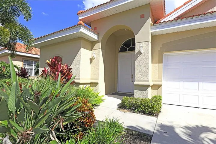 Stucco exterior with an arched entryway, double front doors featuring a semi-circular transom window, and a multi-car garage